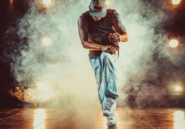 Young cool man break dancing in club with lights and smoke. Tattoo on body.